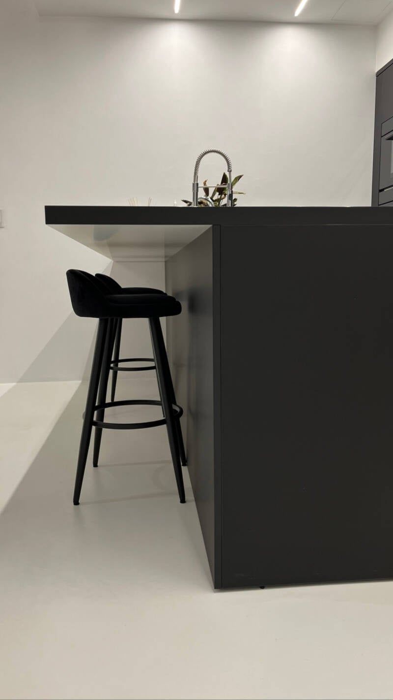 Isola da cucina nera con due sgabelli da bar e un lavello contro una parete bianca.
