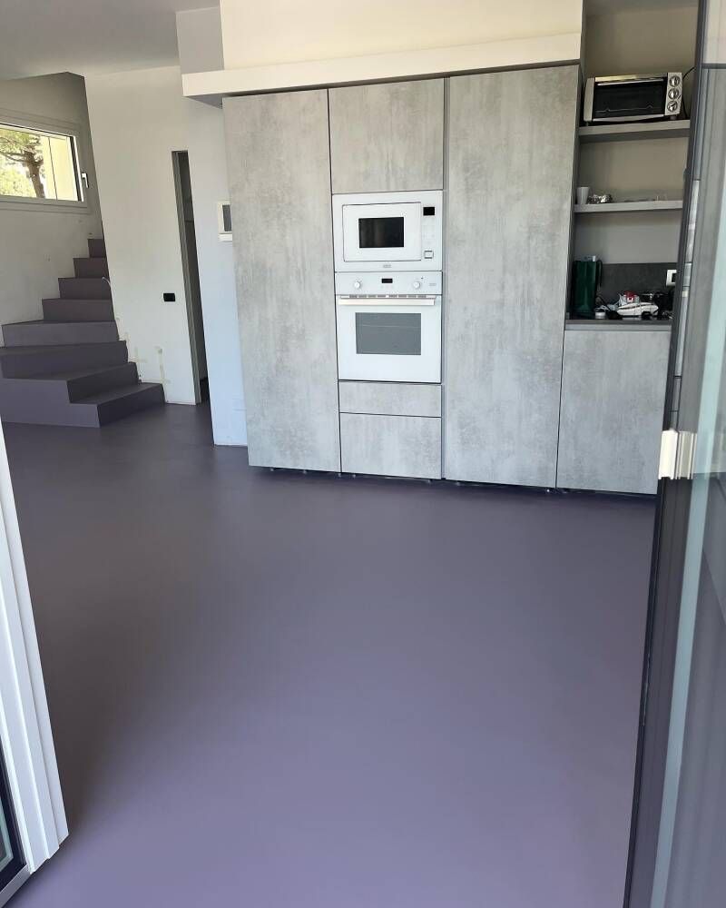 Cucina con mobili grigi, forno e microonde. Pavimento e scale color lavanda.