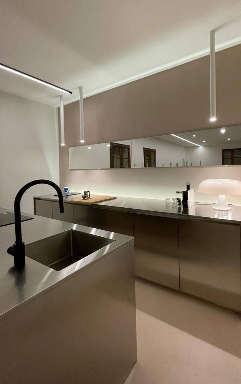 Moderna cucina in acciaio inox con isola, lavello, rubinetto nero e illuminazione dall'alto.