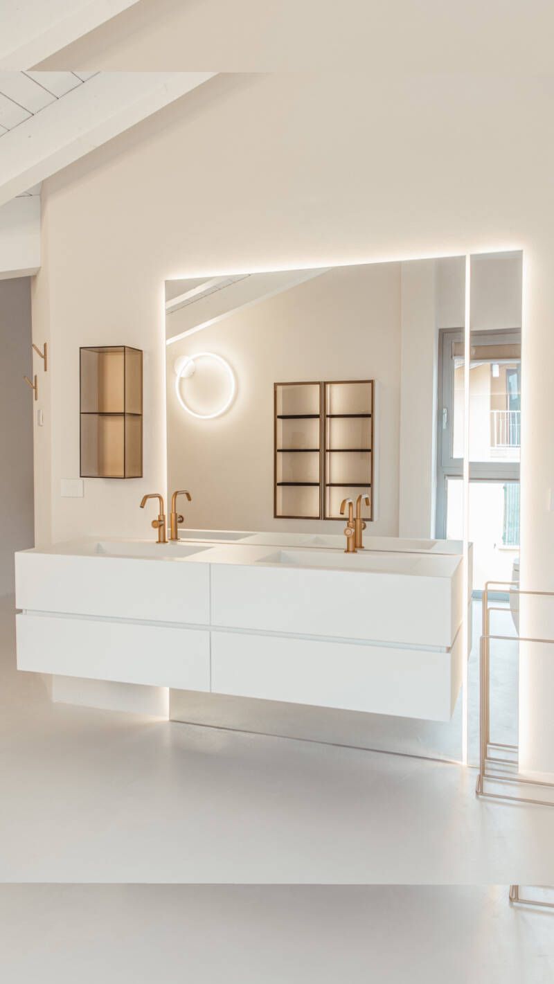 Moderno bagno bianco con doppio lavabo sospeso, grande specchio e dettagli dorati.