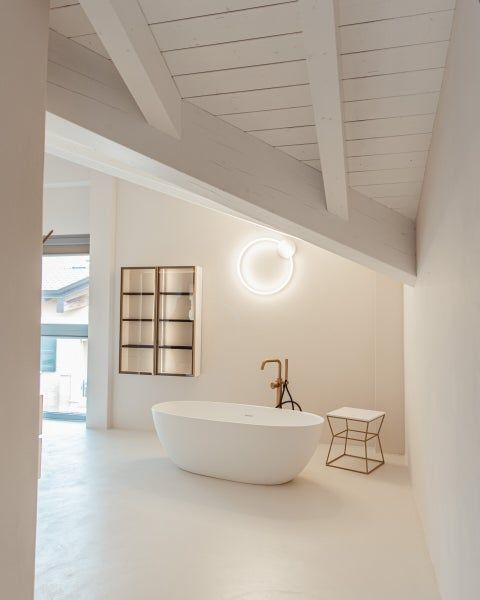 Ampio bagno completamente bianco con una moderna vasca ovale e una lampada circolare sulla parete.