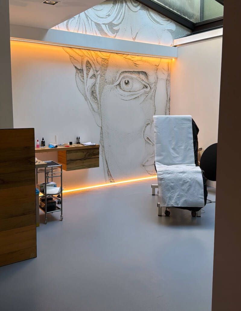 Studio di tatuaggi con un grande murale di David, illuminato da luci calde. Una sedia sterile è in primo piano.