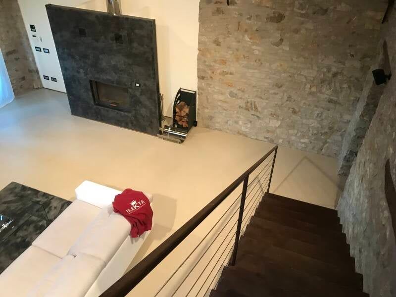 Vista interna: camino, pareti in pietra, scale e un divano con una coperta rossa.