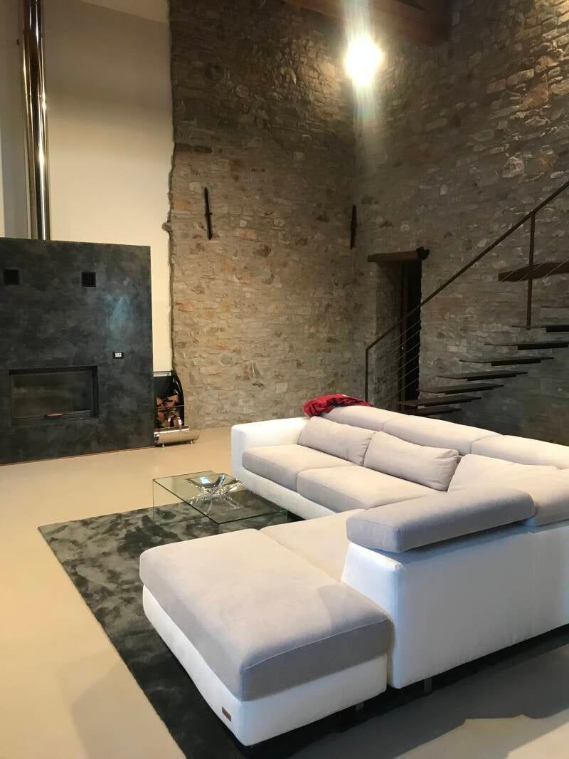 Soggiorno moderno con parete in pietra, divano componibile bianco e tappeto scuro.