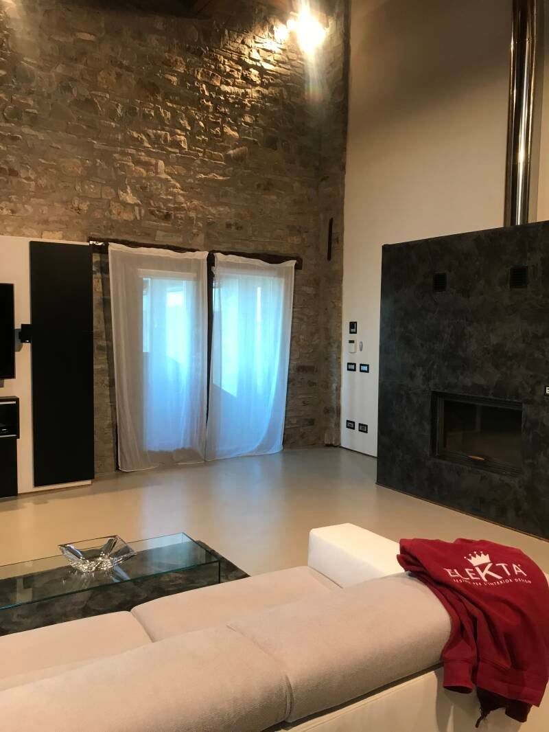 Soggiorno con parete in pietra, camino, tavolino in vetro, divano bianco e tende trasparenti.