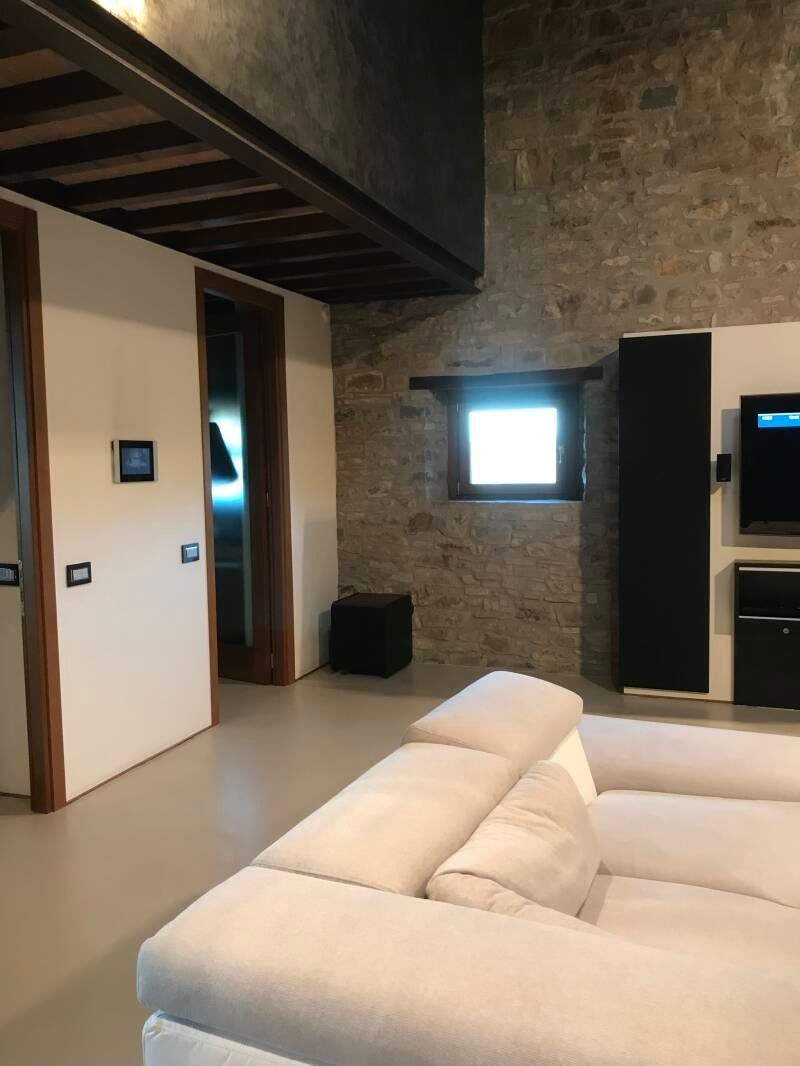 Soggiorno con parete in pietra, divano chiaro e porte con cornice in legno.