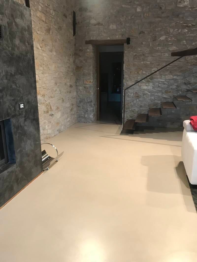 Una stanza con pareti in pietra, pavimento color marrone chiaro, un camino grigio scuro e una scala.