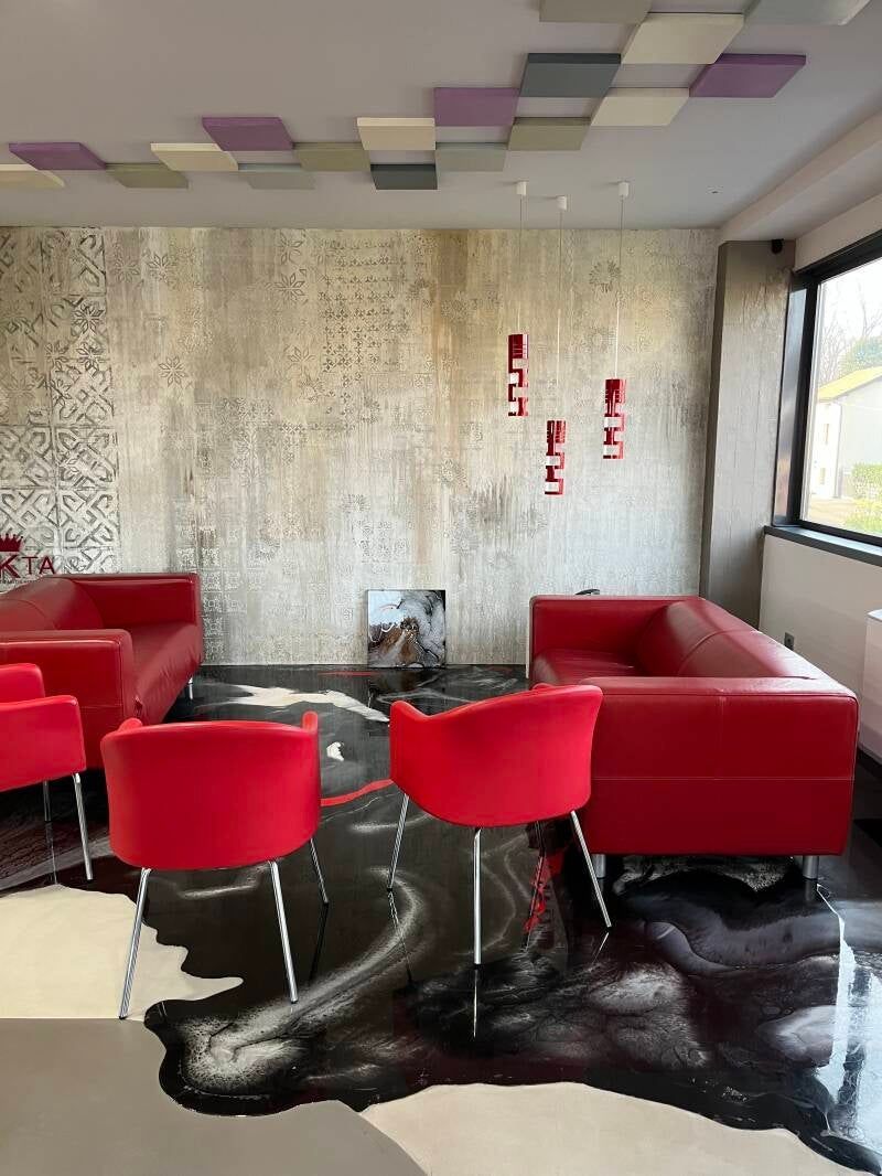 Sedute in pelle rossa in una sala moderna con pavimento artistico in bianco e nero, pareti strutturate e piastrelle colorate sul soffitto.