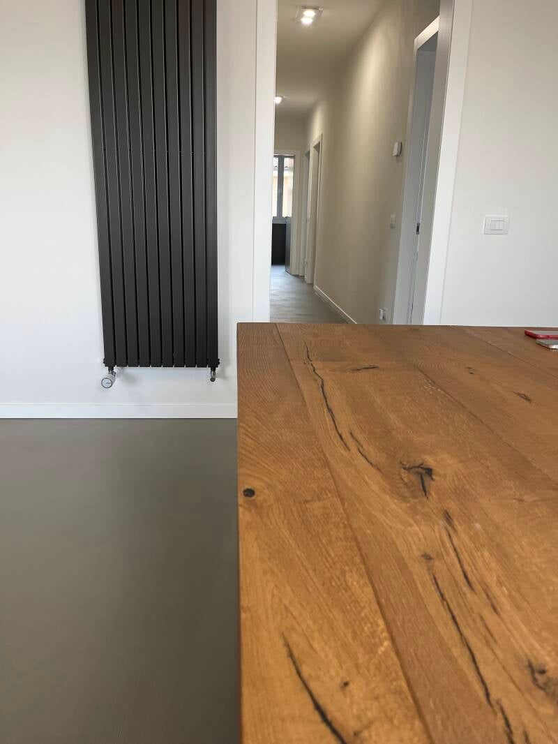 Un corridoio con un tavolo di legno in primo piano, un termosifone scuro e pareti bianche.