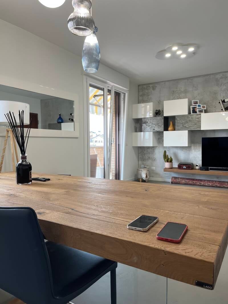 Sala da pranzo con tavolo in legno, telefoni, arredamento moderno e porta-finestra sul balcone.