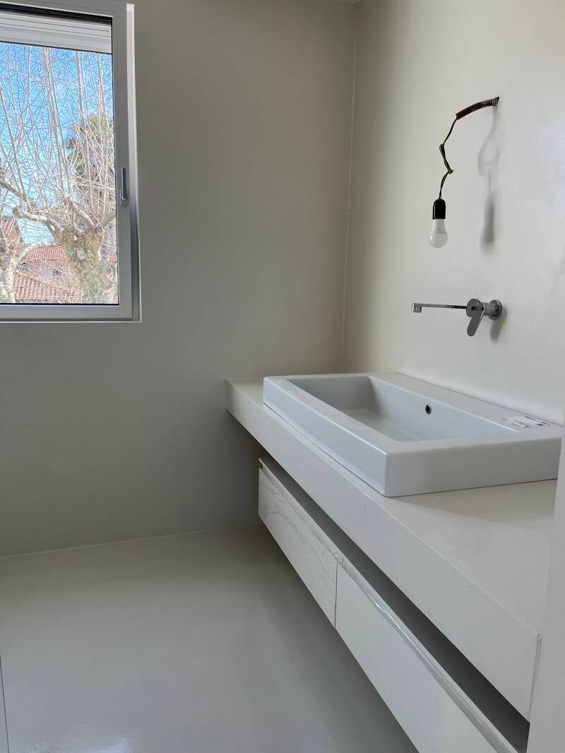 Bagno bianco con lavandino, mobili, finestra e lampada a parete.