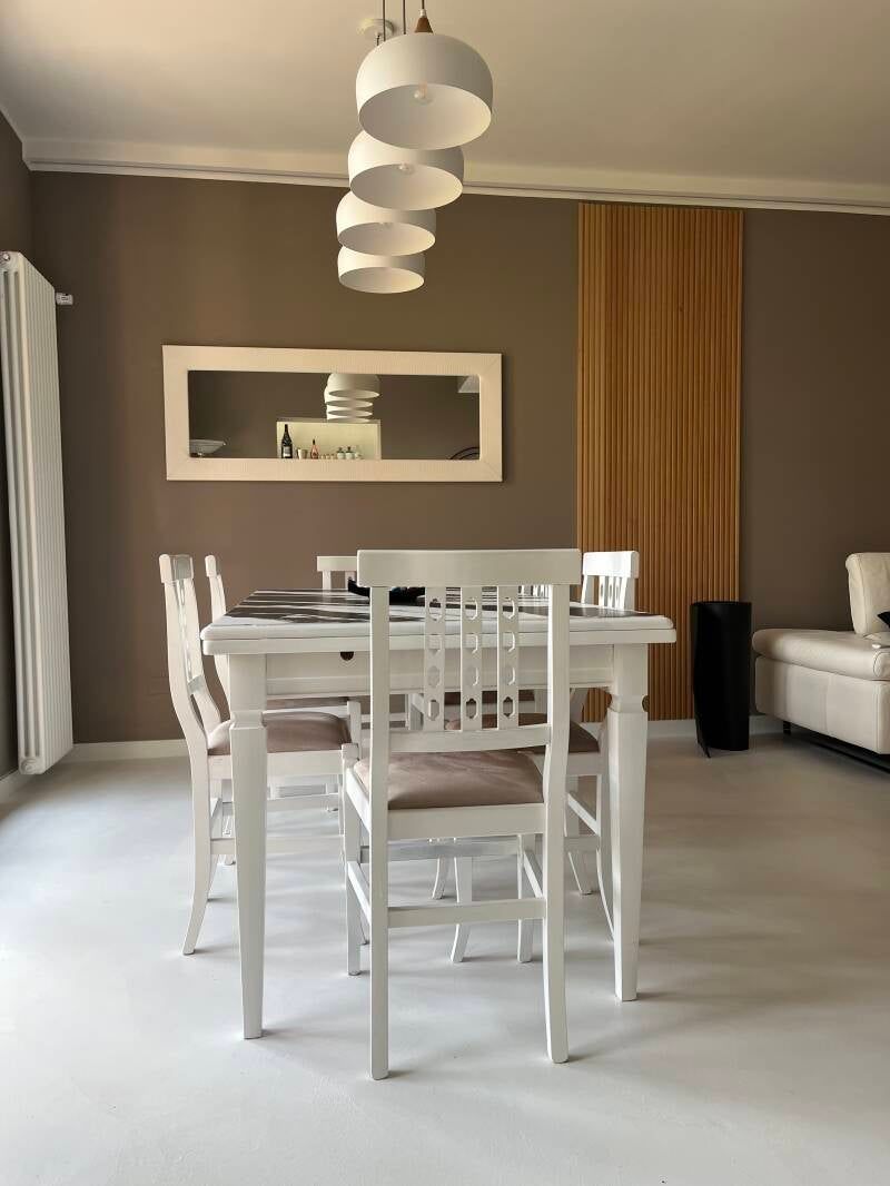 Set da pranzo bianco in una stanza con pareti marroni e pavimenti bianchi, sotto una fila di lampade a sospensione.