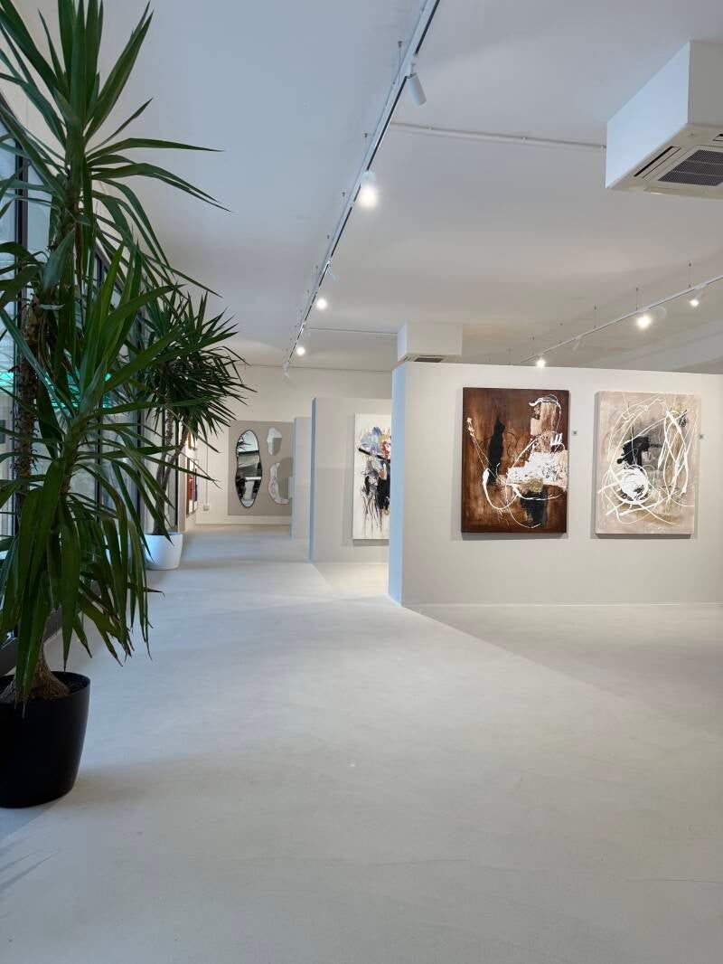 Interno di una galleria d'arte con pareti e pavimento bianchi, opere d'arte e una grande pianta in vaso.