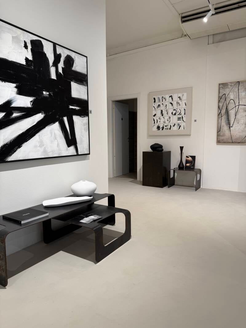 Interno di una galleria d'arte con dipinti astratti in bianco e nero e mobili moderni.