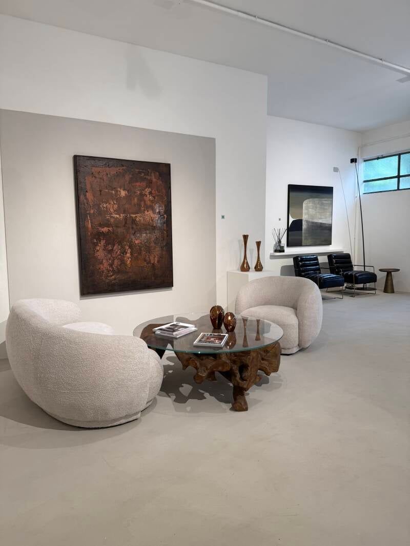 Interno della galleria con opere d'arte astratte, sedie in bouclé bianco e un esclusivo tavolino da caffè in legno.