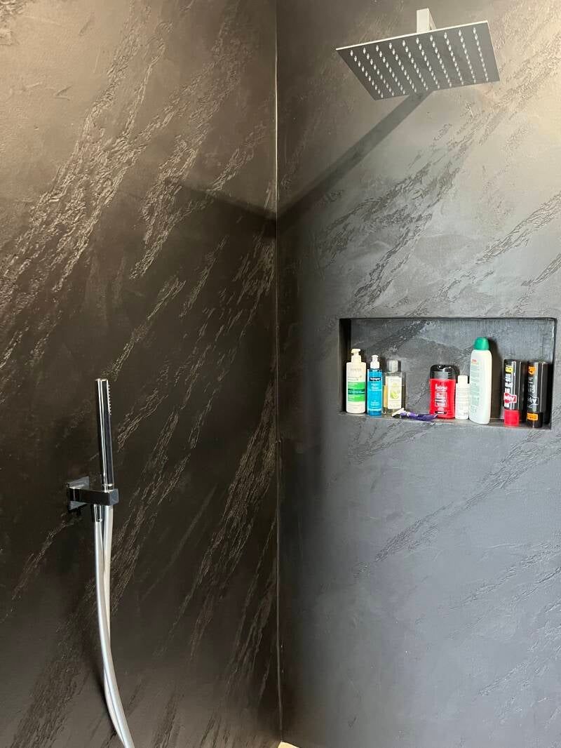 Doccia piastrellata scura con mensola integrata per articoli da toeletta e soffione.