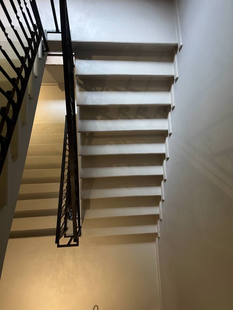 Scala con gradini chiari e ringhiera in metallo scuro che scende dall'alto.