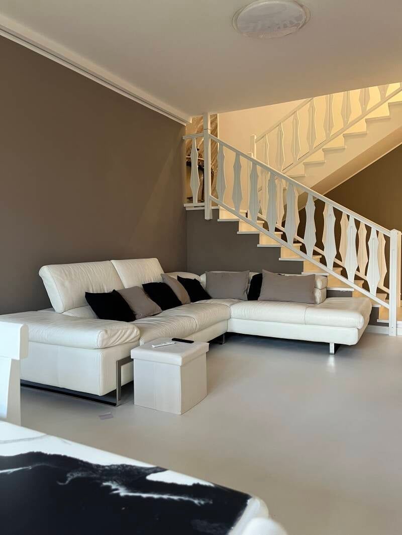 Divano componibile bianco in una stanza con scala bianca, pareti marroni e pavimento bianco.