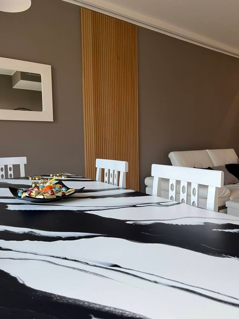 Sala da pranzo con un moderno tavolo con motivi bianchi e neri, sedie bianche e tende color cuoio.