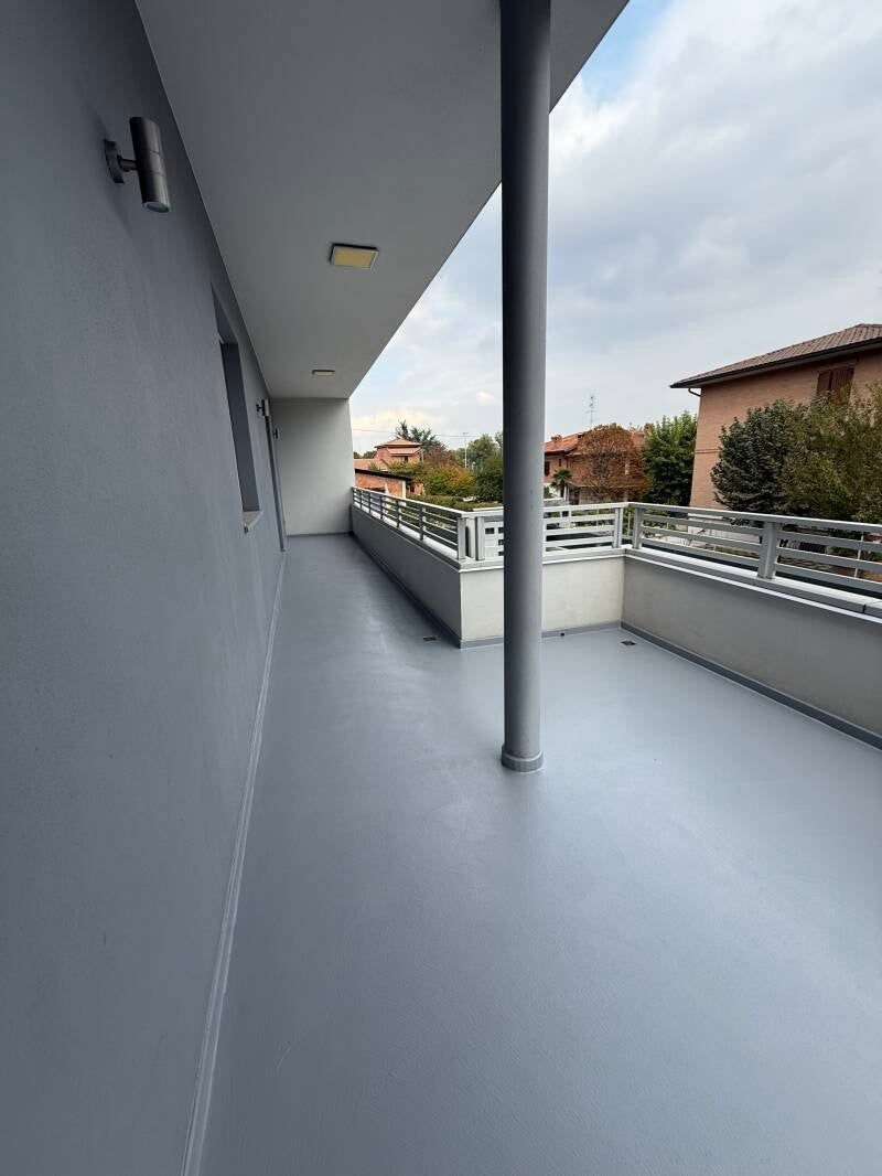 Balcone grigio con colonna, ringhiera e vista sulle case e sul cielo.