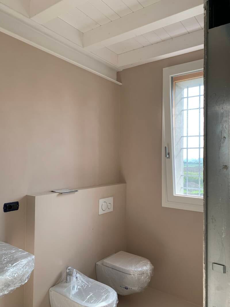 Bagno con pareti beige, soffitto bianco, WC, bidet e finestra.