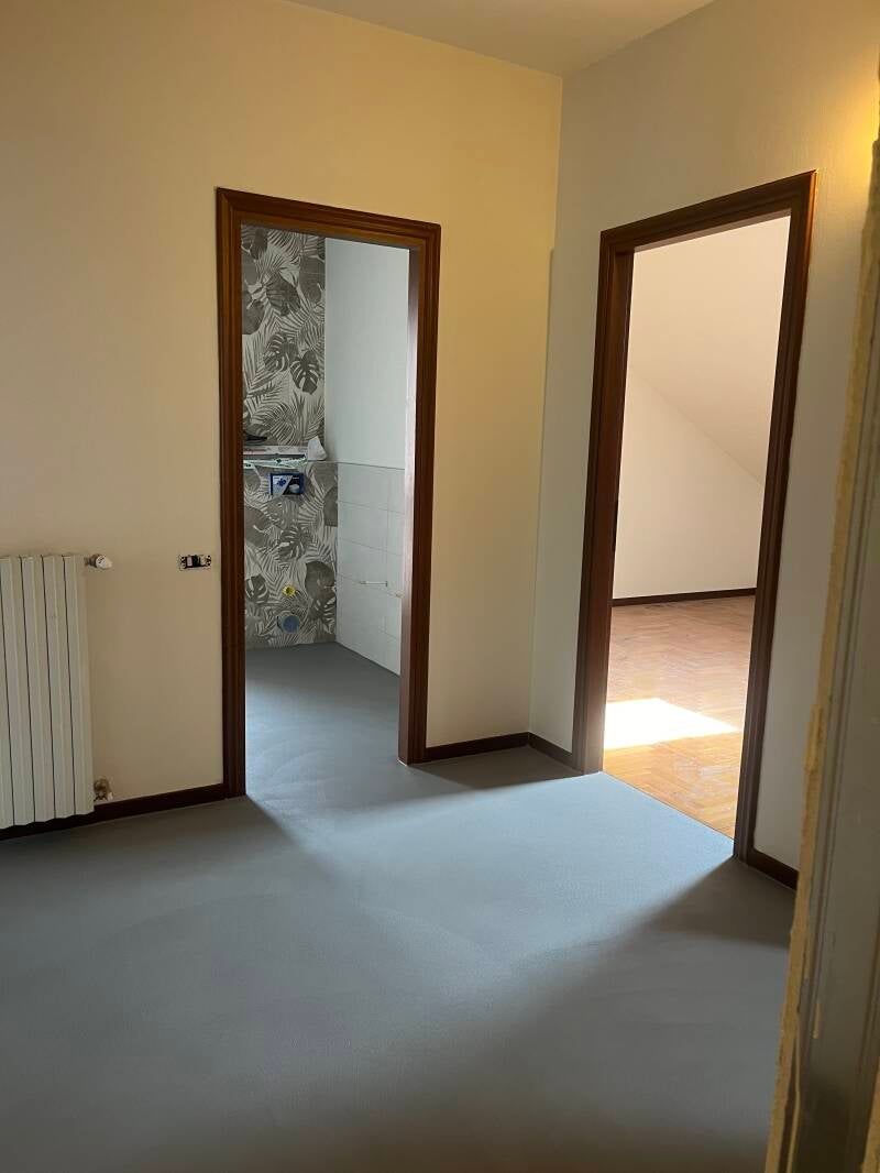 Vista interna con tre ingressi: bagno, soggiorno e corridoio, pavimento grigio.