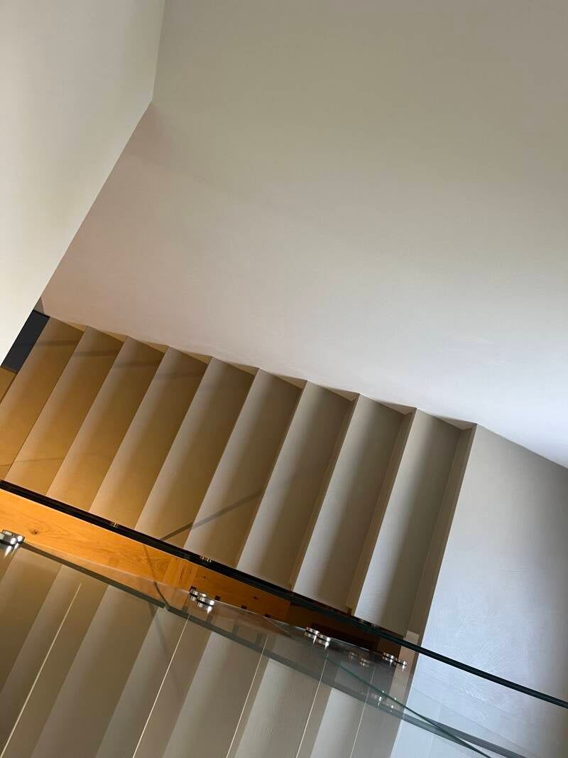 Scala con ringhiera in vetro, corrimano in legno e pareti bianco sporco.