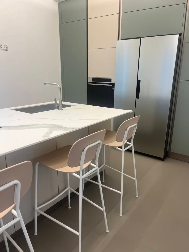 Cucina con piano di lavoro bianco, frigorifero in acciaio inox e tre sgabelli da bar.