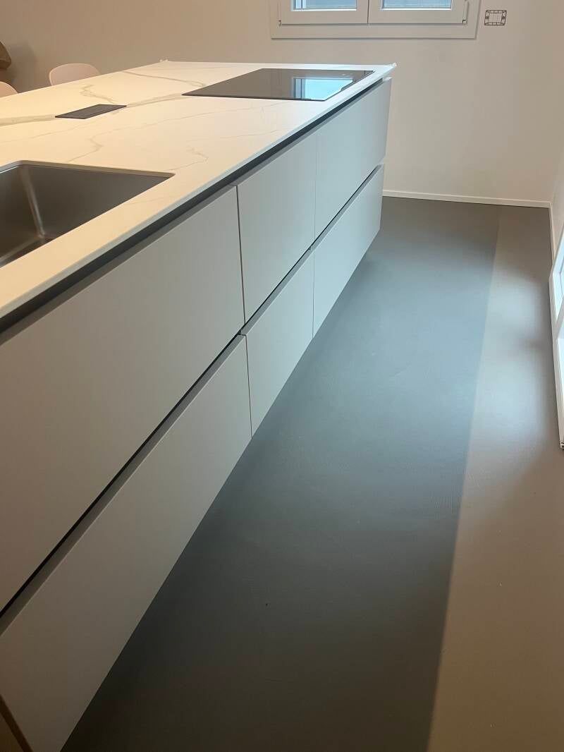 Moderna isola da cucina con mobili e piano di lavoro grigi, pavimento grigio.
