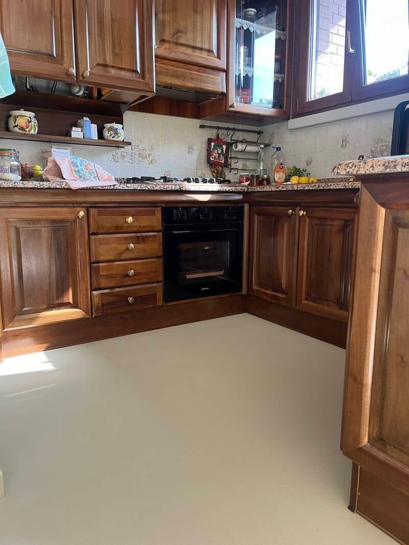 Angolo cottura con mobili in legno, forno e paraschizzi piastrellato. Pavimento chiaro.