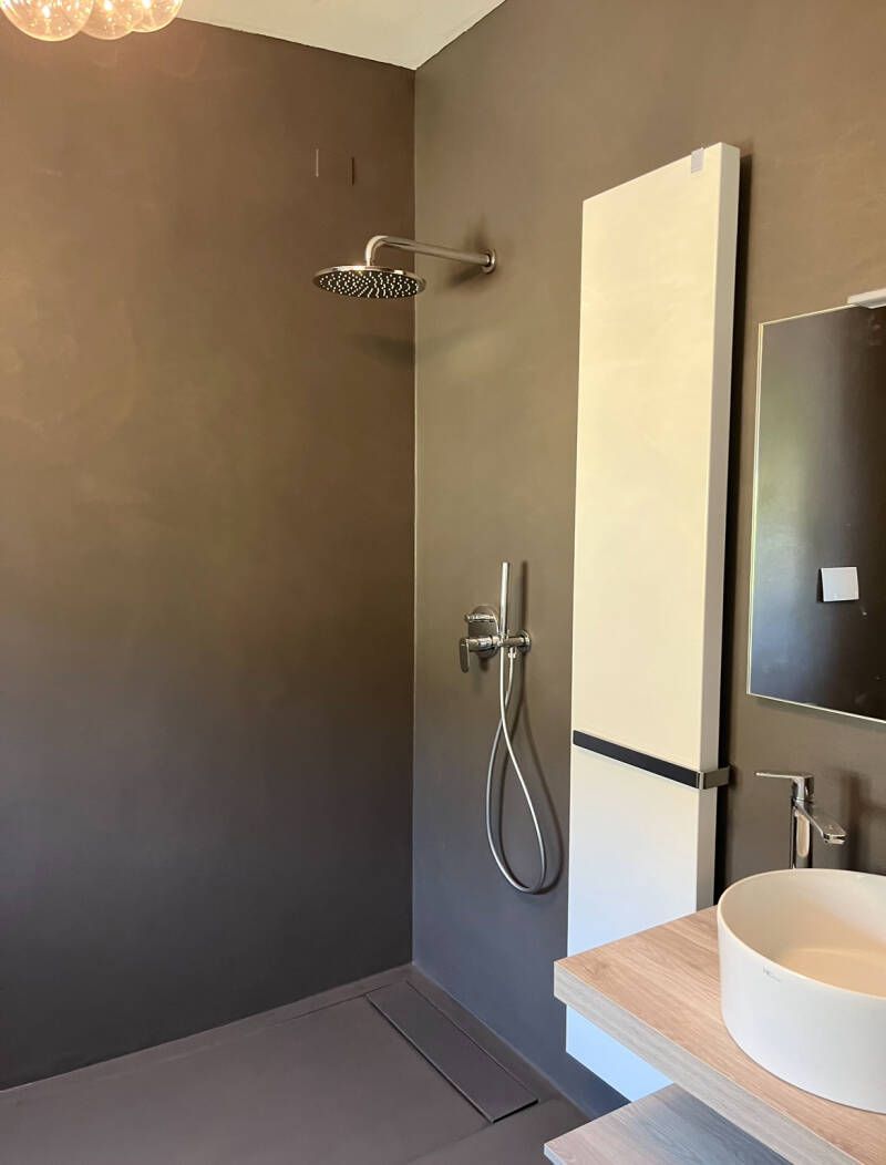 Doccia moderna con pareti grigie, termosifone bianco alto e lavandino rotondo su un ripiano in legno.