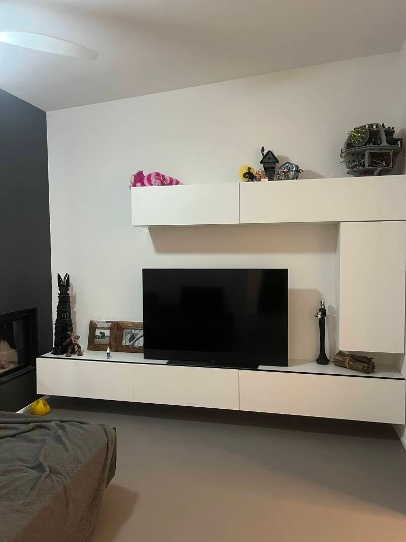 Soggiorno con mobile TV bianco, TV nera e vari oggetti decorativi in ​​mostra. Pavimenti grigi.