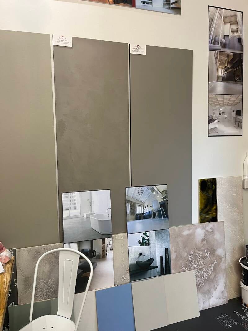 Campioni di colori di vernice, immagini di decorazioni e piastrelle sono esposti su una parete bianca; di fronte c'è una sedia.