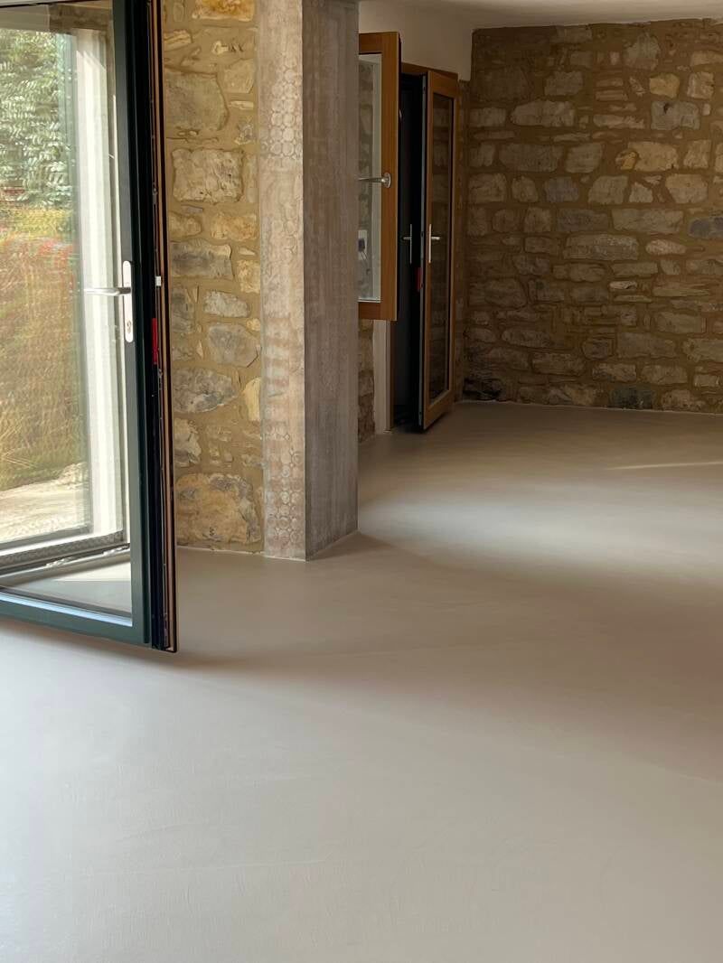 Stanza con pareti in pietra, pavimento grigio chiaro e porte aperte sull'esterno.