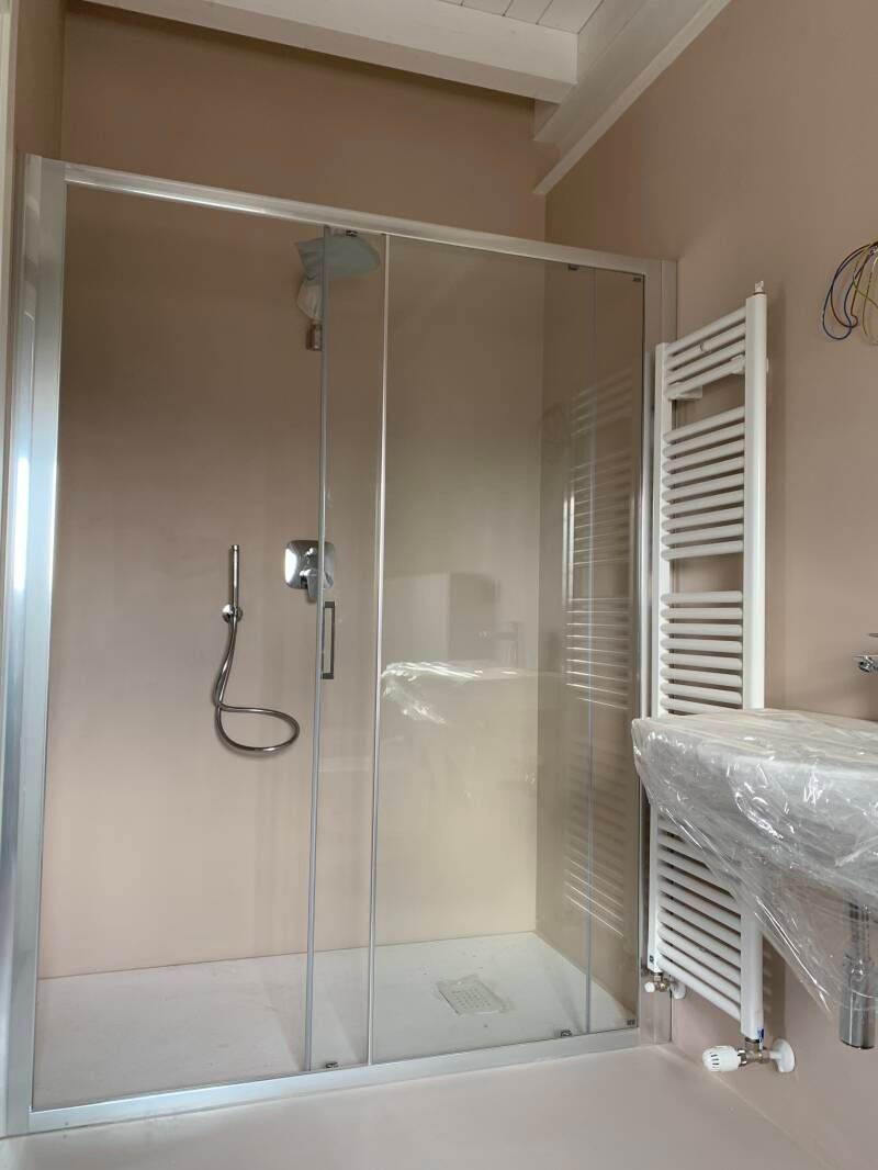 Box doccia con porte in vetro trasparente e accessori cromati in un bagno con pareti rosa pallido.