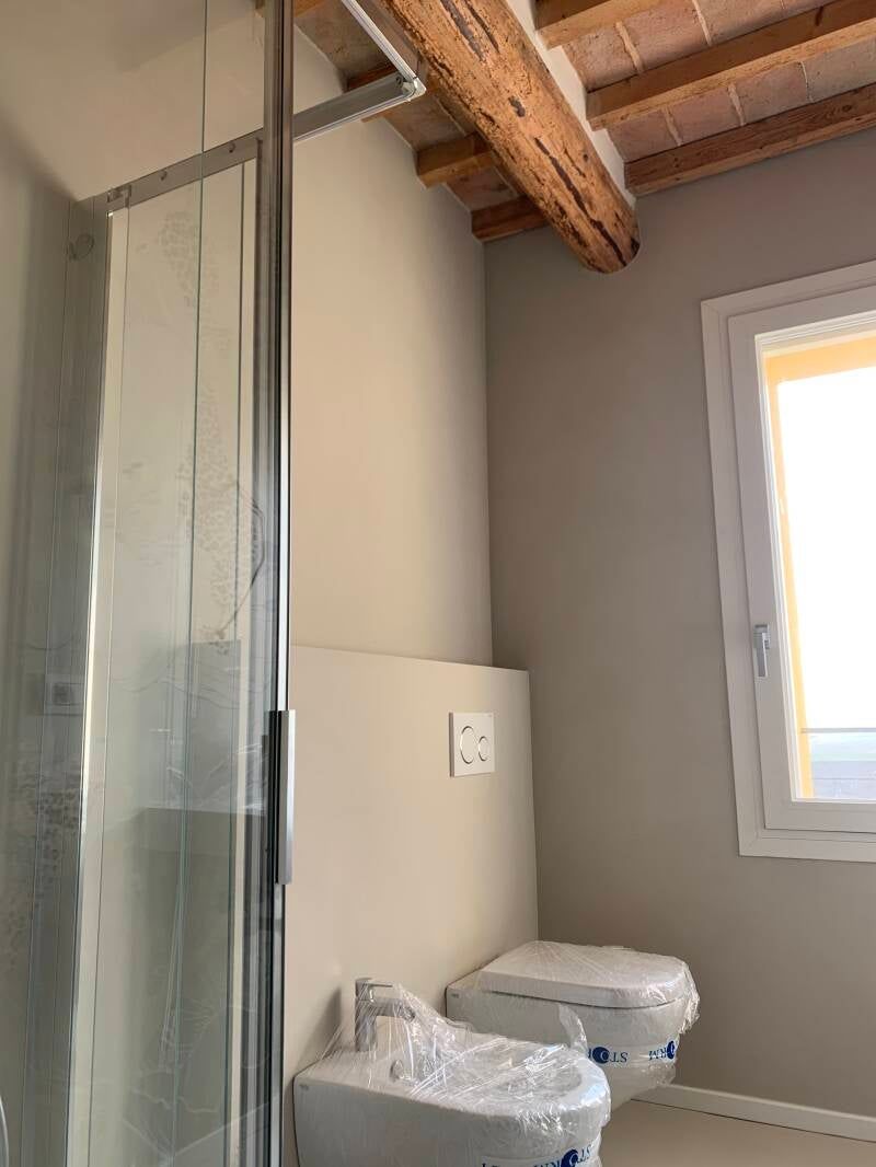 Bagno con doccia, WC, bidet e finestra. Pareti beige e travi in ​​legno a vista.