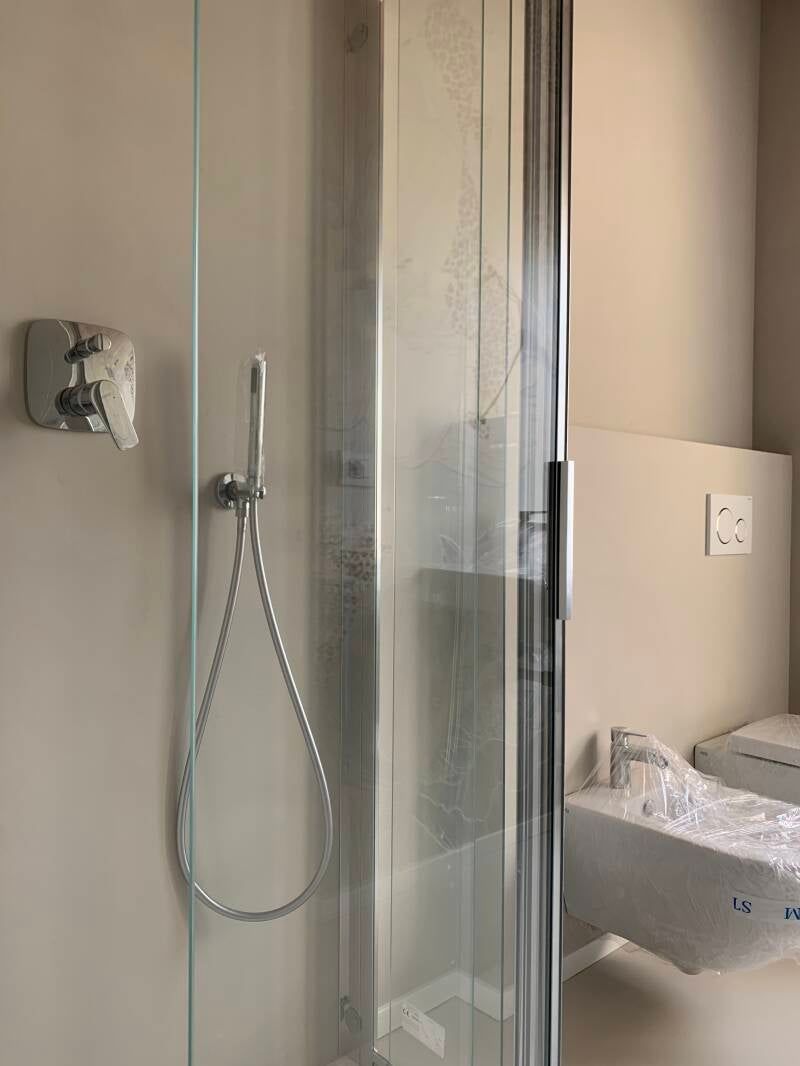 Box doccia con porta in vetro, soffione e bidet in un bagno.