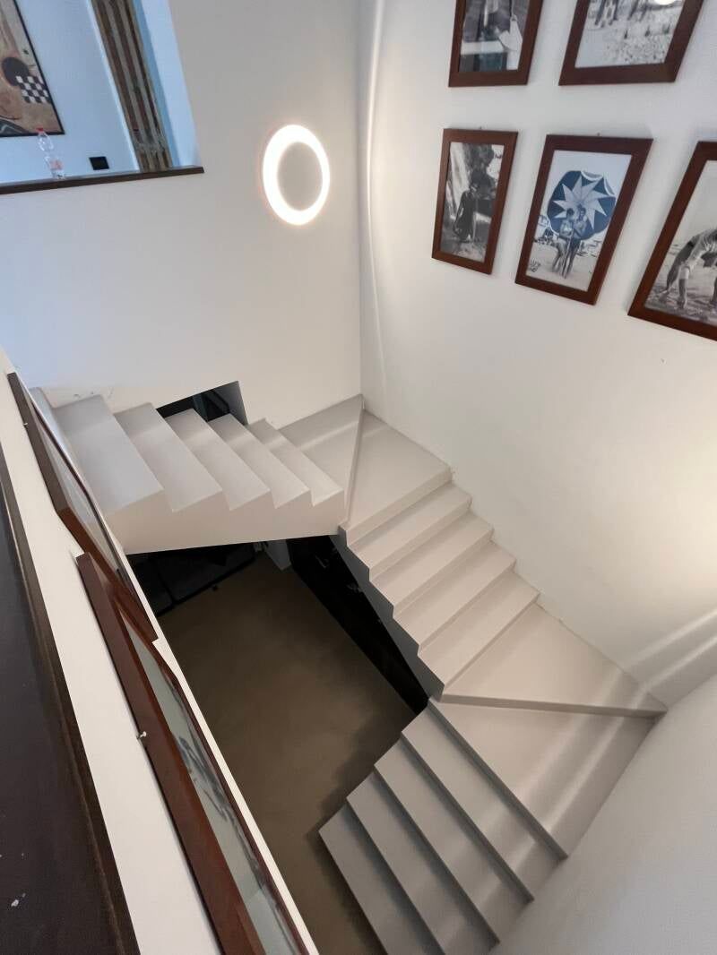 Tromba delle scale con gradini e pareti bianche, foto incorniciate alle pareti e un lampadario circolare.