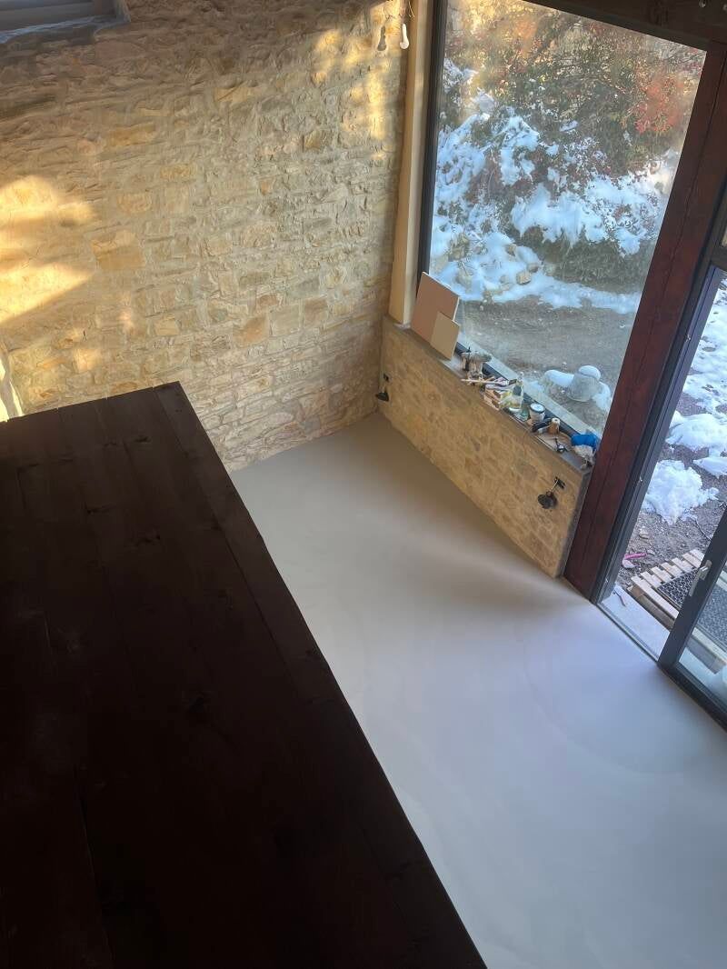 Angolo interno con pavimento grigio chiaro, pareti in truciolato e una finestra con neve all'esterno.