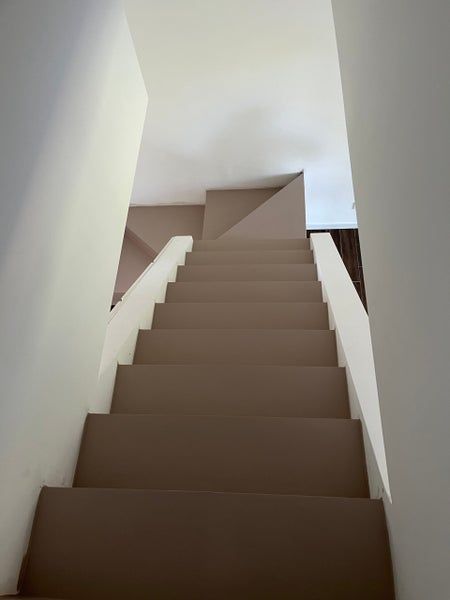Una scala marrone sale tra pareti bianche.