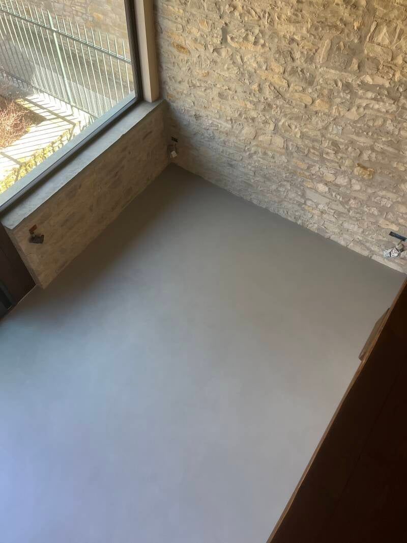 Stanza interna con pavimento grigio, parete strutturata, finestra e superficie in legno.