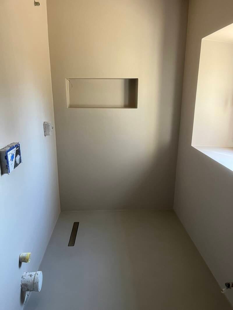 Bagno vuoto con pareti dai colori neutri, mensole incassate e sanitari non finiti.