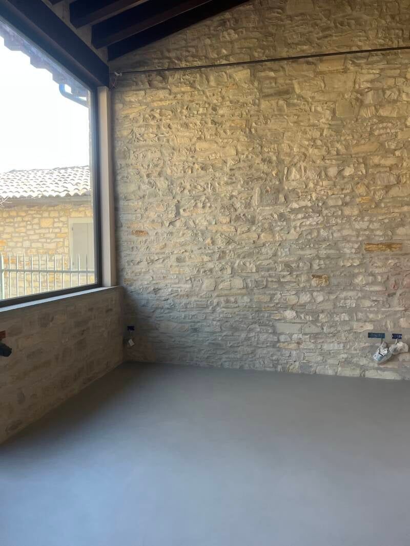 Stanza interna con parete in pietra, finestra e pavimento in cemento grigio.