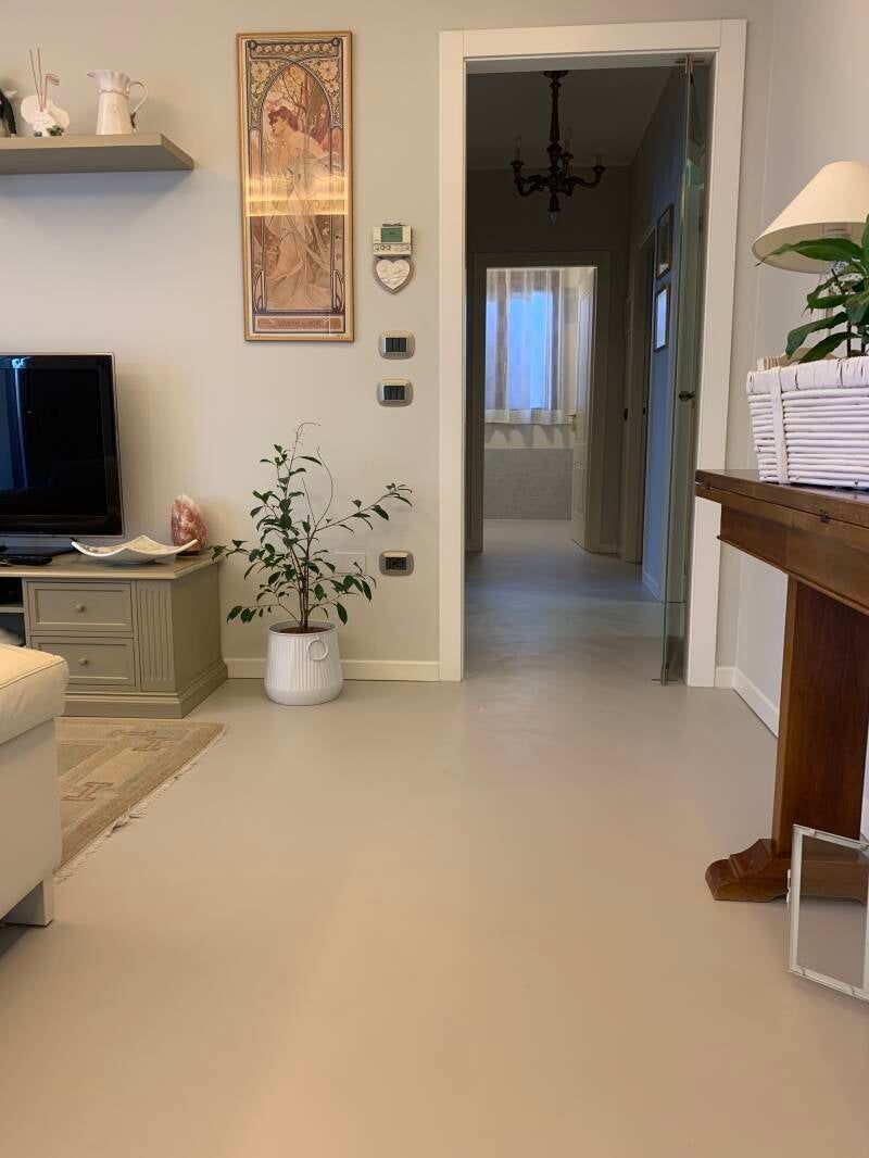 Un soggiorno con pavimenti chiari, un corridoio, una pianta e un quadro incorniciato.