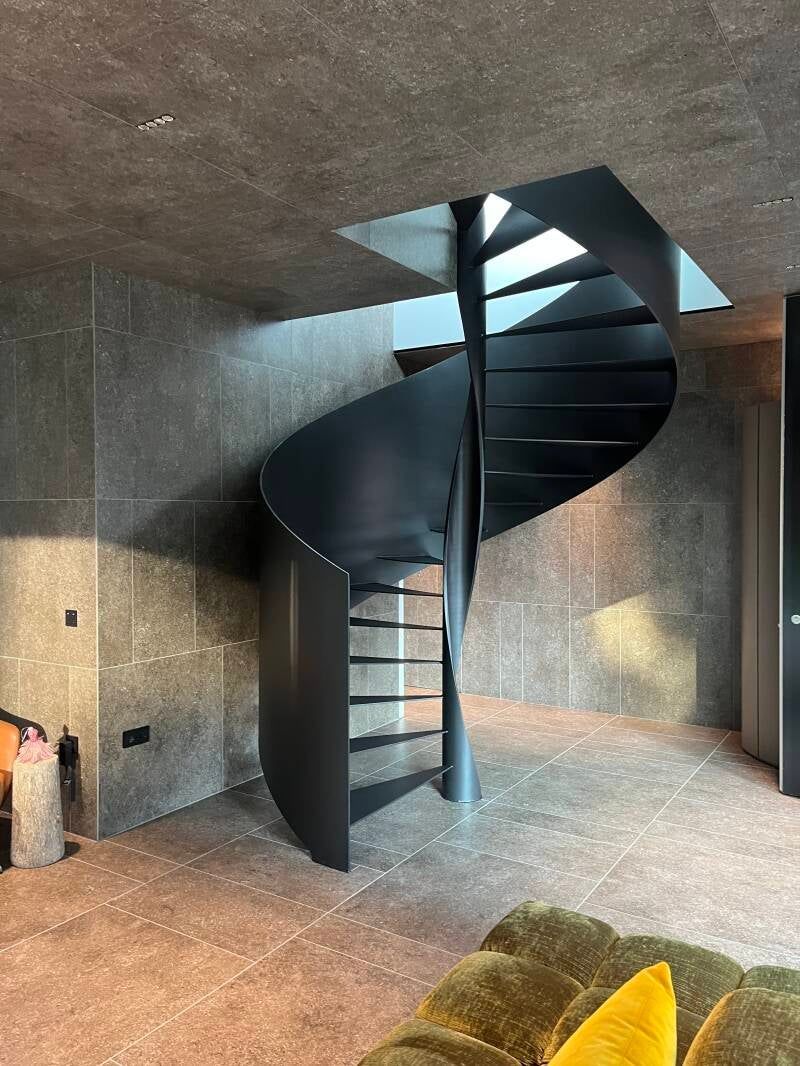 Scala a chiocciola nera in una stanza con pareti e pavimento macchiati di grigio.
