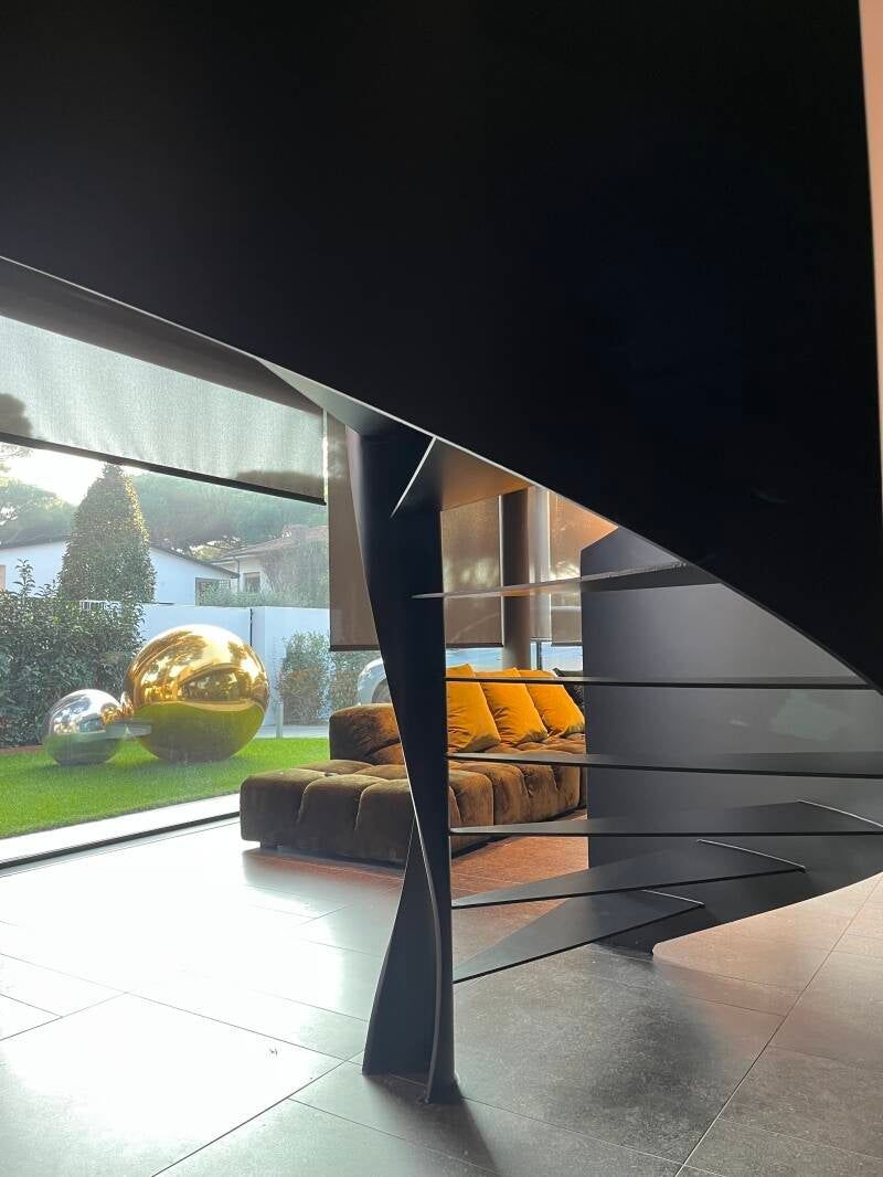 Scala a chiocciola nera in un interno moderno con sfera dorata nella vista del giardino.
