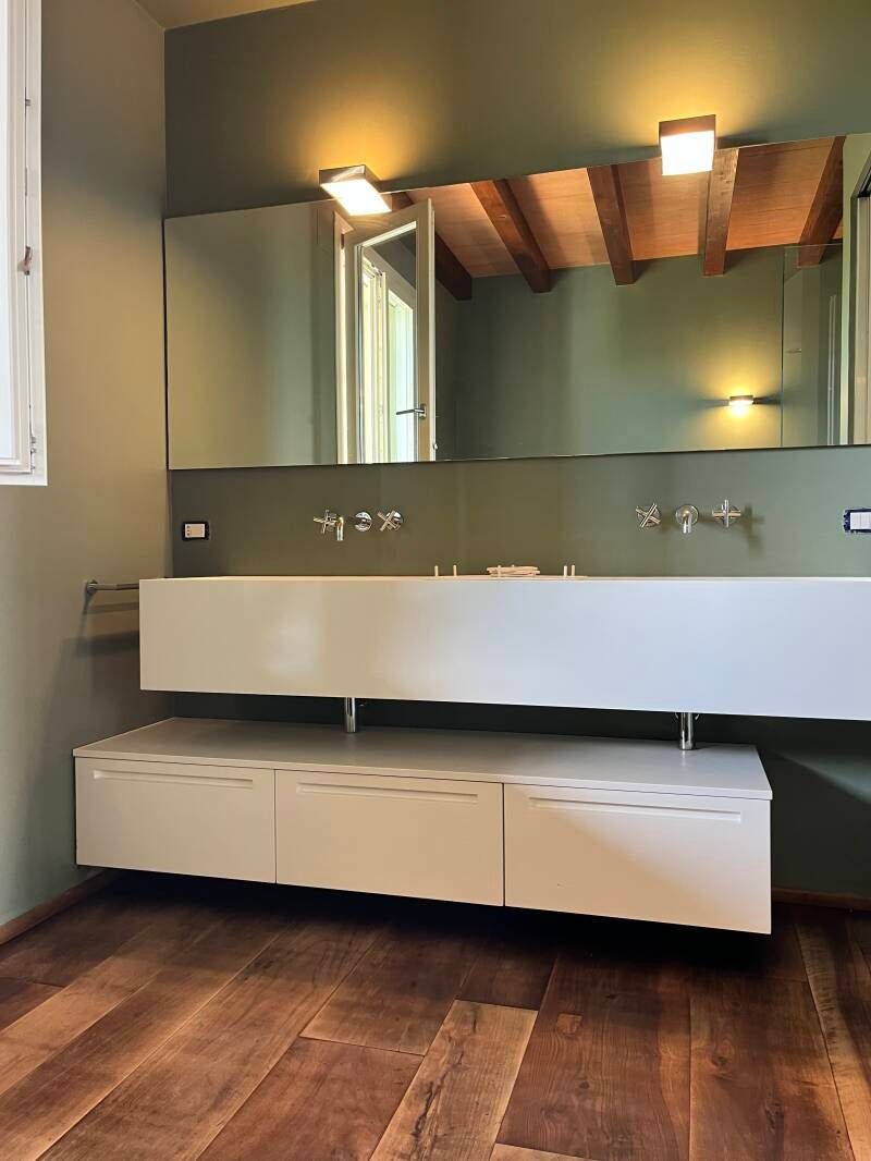 Bagno moderno con doppio lavabo bianco, grande specchio e pareti verdi. Pavimento e soffitto con travi in ​​legno.