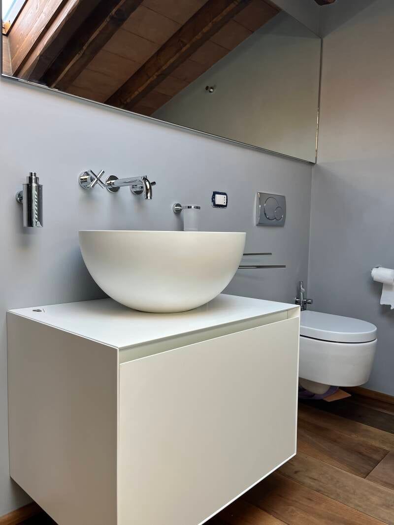Bagno moderno con lavabo bianco su mobiletto bianco, sanitari argentati e WC sospeso.