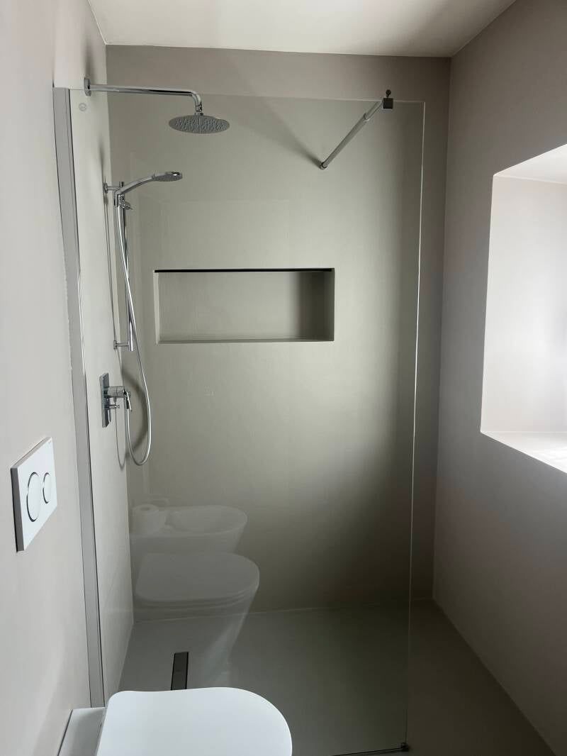 Bagno moderno con doccia in vetro, WC, mensola incorporata e piccola finestra.