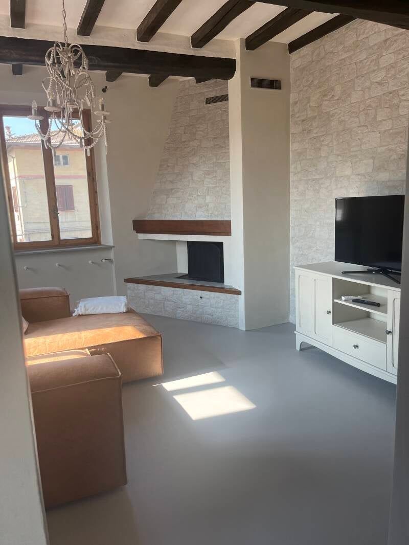 Soggiorno con camino, TV, mobile bianco, divano marrone e finestra con luce solare.